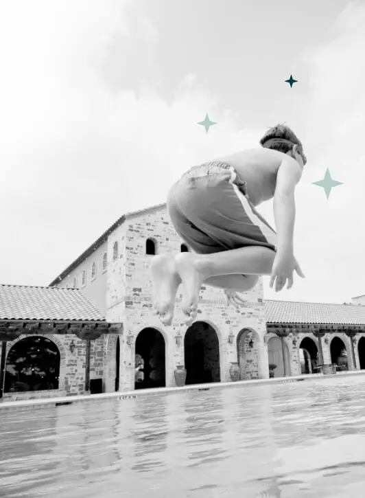 A black and white image of a boy jumping into a swimming pool.