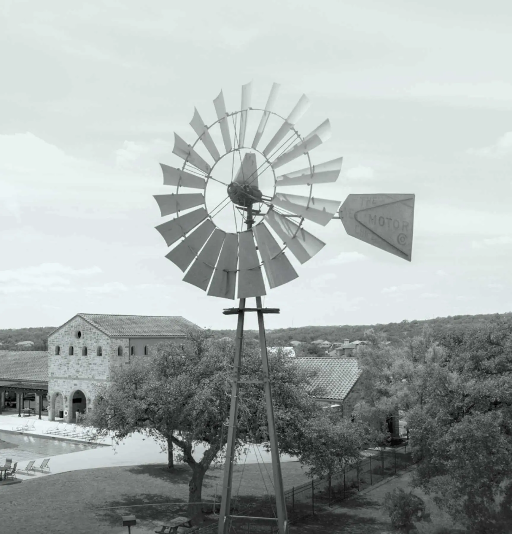 A black and white photo of a windmill in front of a pool.