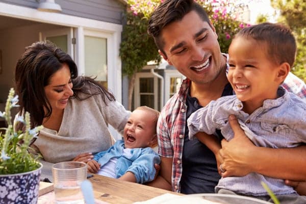 A family is laughing at a table in their backyard.
